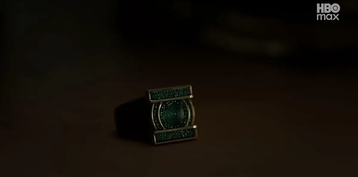 Cincin berwarna hijau dengan desain futuristik bercahaya redup di atas permukaan gelap, menampilkan nuansa misterius.